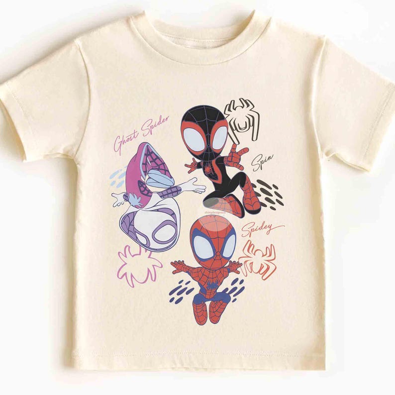 Op de afbeelding: Cr&egrave;mekleurig T-shirt met cartoon illustraties van Spider-Man personages. Het shirt toont Ghost Spider, Spin en Spidey, met hun namen in cursief. Het ontwerp gebruikt rood, zwart, blauw en paars.