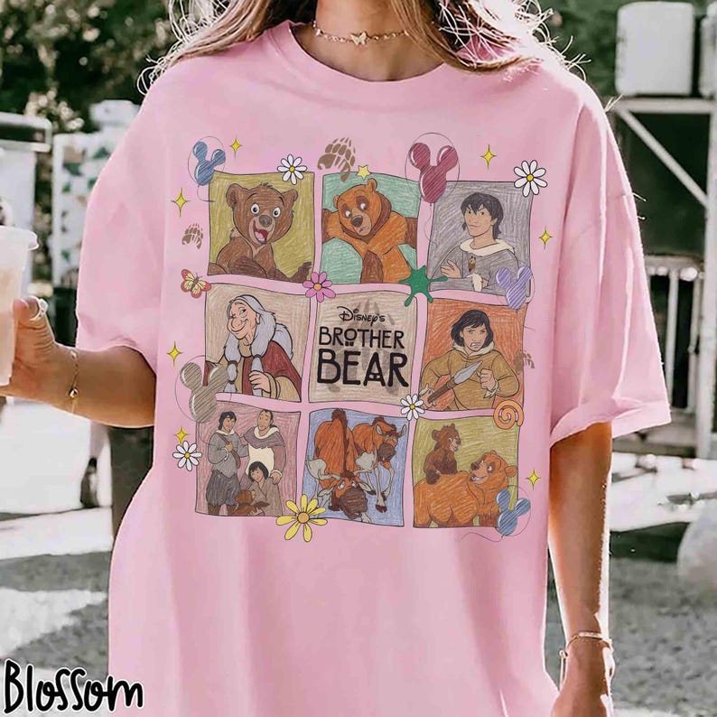 K&ouml;nnte beinhalten: Hellrosa T-Shirt mit einem farbenfrohen Grafikdesign von Disneys "B&auml;renbr&uuml;der". Das Design zeigt Charaktere und Szenen aus dem Animationsfilm, angeordnet in einem Raster. Das Wort "Blossom" ist unten links aufgedruckt.