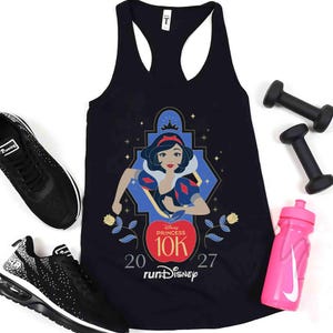 May include: A black racerback tank top featuring a graphic of Snow White inside a blue frame, with the text Disney Princess 10K 2027 runDisney. The tank is surrounded by two black dumbbells, two black and white athletic sneakers, and a pink water bottle.