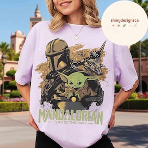 Puede incluir: Una camiseta lila con un gr&aacute;fico de The Mandalorian y Grogu de Star Wars. El dise&ntilde;o incluye el texto "MANDALORIAN - THIS IS THE WAY" en verde y blanco.