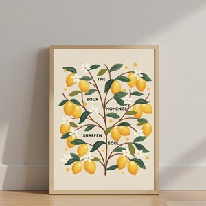 Puede incluir: Una impresión artística enmarcada con una ilustración de un limonero. La obra muestra limones amarillos, hojas verdes y flores blancas sobre un fondo crema. El texto en la impresión dice "The Sour Moments Sharpen Soul."