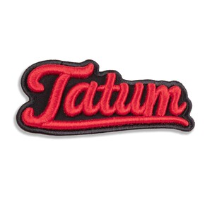 May include: An embroidered patch featuring the name Tatum in bright red, cursive-style thread. The lettering is outlined in a thick black border, creating a bold contrast against the red text. The patch has a distinct, raised texture throughout.