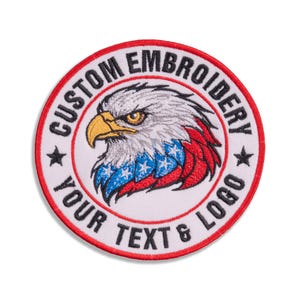 May include: A circular embroidered patch featuring a bald eagle head with a yellow beak and feathers patterned in red, white, and blue. The text CUSTOM EMBROIDERY and YOUR TEXT & LOGO is stitched in black along the white border with two black stars.