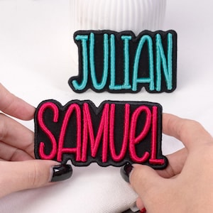 May include: Two embroidered patches with names. One patch says "JULIAN" in turquoise letters with a black border. The other patch says "SAMUEL" in red letters with a black border. Both patches are rectangular.