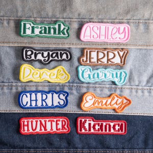 May include: A collection of ten embroidered name patches featuring various fonts and colors, including Frank in green, Ashley in pink, Bryan in black, Jerry in brown, Derek in yellow, Garry in light blue, Chris in blue, Emily in orange, Hunter in red, and Kian in red.