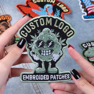 May include: Embroidered patch with a green cannabis bud character wearing sunglasses and a smiling face. The patch has the words "CUSTOM LOGO" and "EMBROIDERED PATCHES" in white lettering on a black background.