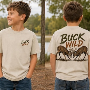 May include: A beige short-sleeve t-shirt featuring the text BUCK WILD on the front left chest. The back of the shirt displays a large graphic of two deer locking antlers with the text BUCK WILD printed in a distressed font above the illustration.