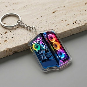 May include: A clear acrylic keychain featuring a miniature computer case design. The case has a blue and black interior with colorful LED lights. The keychain includes a silver metal ring and chain.