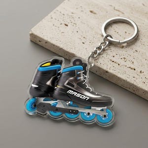 May include: A clear acrylic keychain featuring a detailed illustration of a black and blue inline skate. The keychain has a silver chain and ring. The word "MASON" is printed on the side of the skate.