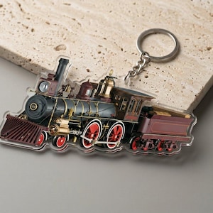 May include: A detailed keychain featuring a vintage steam train. The train is primarily black, maroon, and gold, with red wheels. The keychain has a silver chain and ring. The image is set against a neutral background.