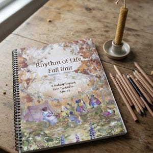 May include: A spiral-bound curriculum book titled Rhythm of Life Fall Unit, featuring a watercolor illustration of figures in a forest setting, accompanied by a collection of colored pencils and a single beeswax candle in a small ceramic holder.