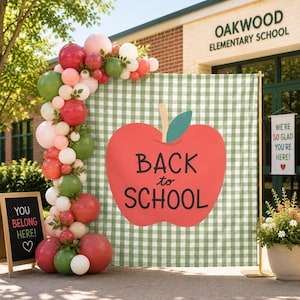 May include: A square backdrop featuring a green and white gingham pattern with a large red apple graphic and the text BACK to SCHOOL. A balloon garland in shades of red, pink, and green is attached to the left side. A small chalkboard sign reads YOU BELONG HERE!