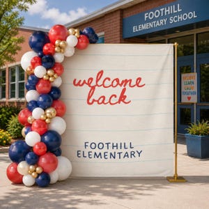 Könnte beinhalten: Ein großer rechteckiger Hintergrund mit einem weißen linierten Papierdesign, dem roten Schriftzug welcome back und dem blauen Text FOOTHILL ELEMENTARY. Eine Ballongirlande in Rot, Marineblau, Weiß und Metallic-Gold schmückt die linke Seite.