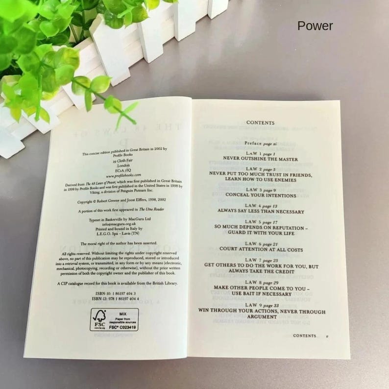 May include: An open book with the title "Power" at the top. The contents page lists laws including "Never Outshine the Master" and "Conceal Your Intentions". The book is open to a spread of text, with a list of contents.