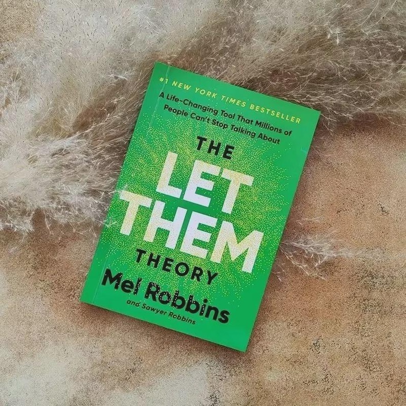 Może przedstawiać: Książka zatytułowana "THE LET THEM THEORY" autorstwa Mel Robbins i Sawyer Robbins. Książka ma jasnozieloną okładkę z białym tekstem i tekstem "#1 NEW YORK TIMES BESTSELLER".