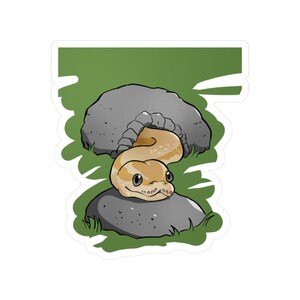 May include: A sticker depicting a cartoon snake in tan and cream tones, smiling and resting on a grey rock. The background shows another grey rock and green grass. The snake is the central focus of the illustration.