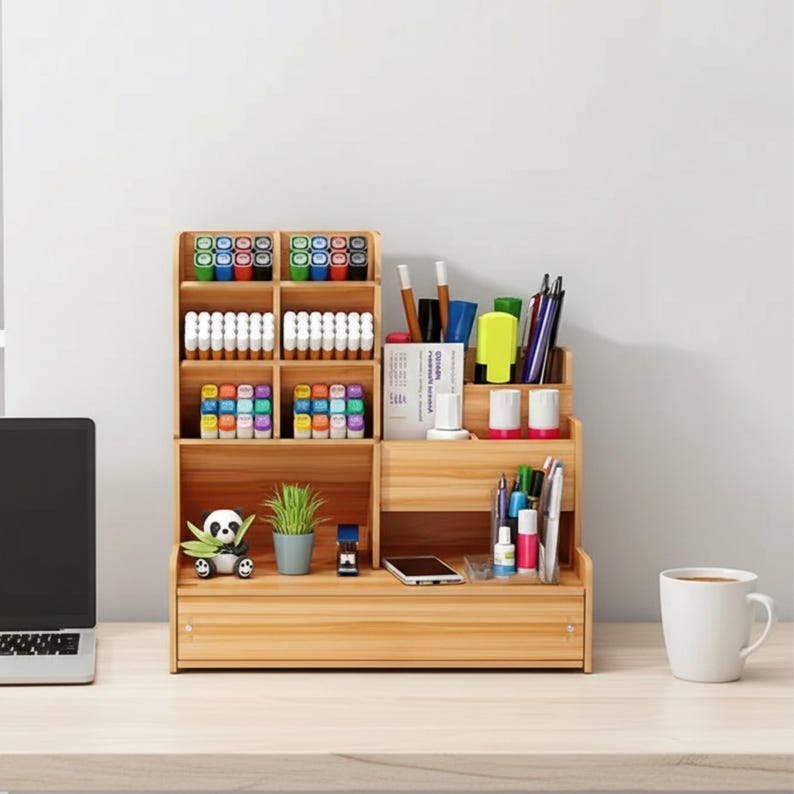 May include: A wooden desk organizer with multiple compartments and drawers. It holds various office supplies, including pens, markers, and small plants. A laptop and a coffee cup are also visible on the desk.
