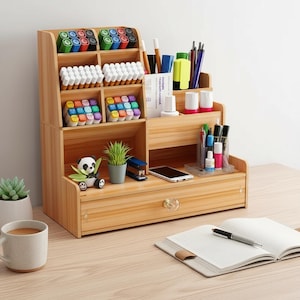 Könnte beinhalten: Ein hölzerner Schreibtisch-Organizer mit mehreren Fächern und einer Schublade. Er enthält verschiedene Kunstmaterialien, darunter Marker, Stifte und Farbtuben. Eine kleine Panda-Figur und eine Topfpflanze sind ebenfalls zu sehen.