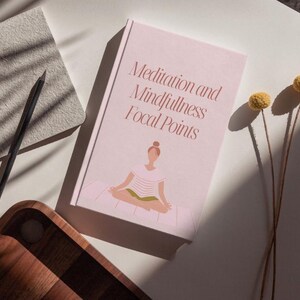 May include: A light pink book titled "Meditation and Mindfulness Focal Points" with an illustration of a person meditating. A notebook, pencil, and wooden tray are also visible. Dried yellow flowers add a natural touch.
