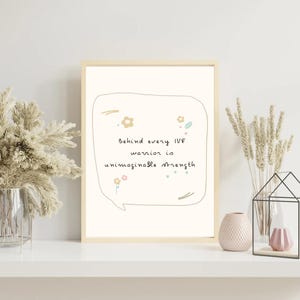 Peut inclure: Une affiche encadrée avec le texte "Behind every IVF warrior is unimaginable strength" dans une bulle de dialogue. L'affiche est dans un cadre beige clair, avec des accents floraux. L'affiche est exposée sur une étagère blanche avec des objets décoratifs.