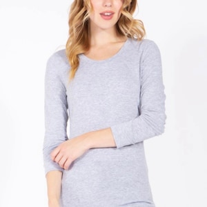 May include: Heather grey long-sleeve shirt with a scoop neck. The shirt is a solid color and has a relaxed fit. The brand logo "Brezy Fashion" is in the upper right corner. The word "PLUS" is in the upper left corner.