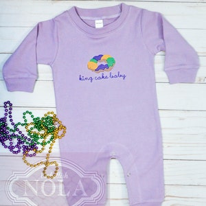 May include: Purple long-sleeve baby onesie with an embroidered king cake and the text "king cake baby".