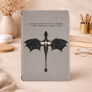 May include: A light gray e-reader case featuring a black dragon illustration with gold-colored wing accents. The text printed above the dragon reads: A dragon without its rider is a tragedy. A rider without their dragon is dead.