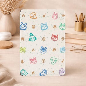 May include: A rectangular tablet case featuring a cream-colored background with a repeating pattern of colorful Animal Crossing character icons and small symbols like houses, trees, and leaves scattered across the surface in various pastel hues.