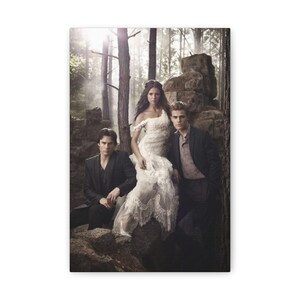 May include: A canvas print featuring three people in a forest setting. A woman in a white, off-the-shoulder dress sits between two men in dark suits. The background includes trees, rocks, and a soft, diffused light.