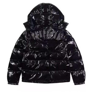 Peut inclure: Veste matelassée noire brillante avec capuche. Le blouson présente un motif matelassé et un logo dans le haut du dos. Le matériau a une finition brillante et réfléchissante. La veste a une fermeture éclair intégrale et des poignets élastiques.