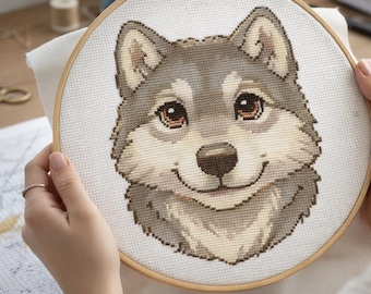 May include: A cross-stitch embroidery of a smiling wolf's face, held in a wooden hoop. The wolf features gray, tan, and brown thread, with detailed eyes and a friendly expression. The craft project is on white fabric.
