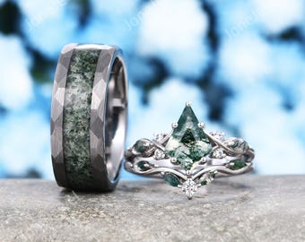 Op de afbeelding: Een donkergrijze, gehamerde metalen ring met een centrale inleg van mosagaat, naast een zilverkleurige ring met een vliegervormige mosagaat als hoofdsteen, geaccentueerd door kleinere markiesgeslepen mosagaatstenen en ronde steentjes.