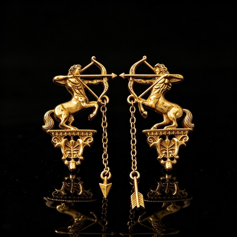 May include: A pair of gold-coloured earrings featuring a centaur with a bow and arrow design. The earrings have a dangling chain with an arrow pendant. The centaur is standing on a decorative base. The background is black.