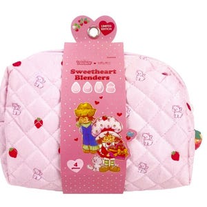 Op de afbeelding: Een lichtroze gewatteerde toilettas met een herhalend patroon van kleine aardbeien en witte kittens. Een roze kartonnen hoes wikkelt zich om het midden, met de tekst Sweetheart Blenders, Strawberry Shortcake en 4 pieces.
