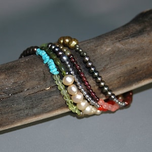 May include: A stack of colorful beaded bracelets with turquoise, green, red, and white beads. The bracelets are on a wooden surface.