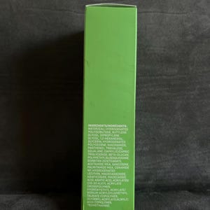 Pu&ograve; includere: Una scatola di prodotto verde con un elenco di ingredienti in testo bianco. Gli ingredienti includono acqua, poliisobutene idrogenato, butilene glicole e glicerina. La scatola &egrave; su una superficie scura.