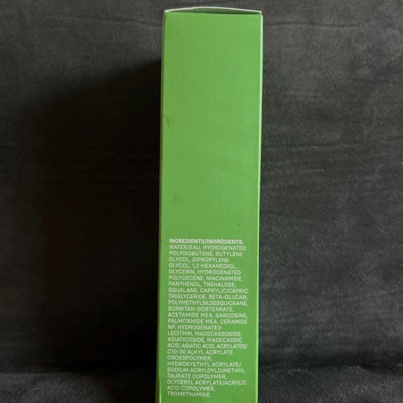 Pu&ograve; includere: Una scatola di prodotto verde con un elenco di ingredienti in testo bianco. Gli ingredienti includono acqua, poliisobutene idrogenato, butilene glicole e glicerina. La scatola &egrave; su una superficie scura.