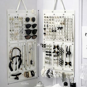 Può includere: Due organizzatori di gioielli bianchi sospesi, ciascuno con più scomparti per orecchini, collane, occhiali da sole e accessori per capelli. Gli organizzatori sono larghi 34.9 cm e alti 66 cm, con una varietà di gioielli e accessori.