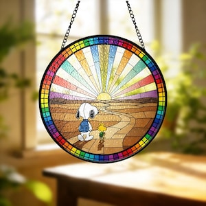 May include: Round stained glass window featuring Snoopy and Woodstock walking towards a sunset. The window has a rainbow border and a black metal frame. The background depicts a colorful sky and a brown landscape.