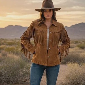 May include: A brown suede fringe jacket with a matching brown hat and blue jeans. The jacket has long fringe on the sleeves and chest. The person is wearing brown cowboy boots. The background is a desert landscape.