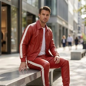 May include: A red leather jacket and trousers set with white stripes. The outfit is worn with a white t-shirt and white trainers. The person is seated on a concrete bench in a city environment.