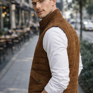 May include: A brown suede vest with a quilted design, featuring two front pockets and a high collar. The vest is worn over a white button-down shirt. A wristwatch with a brown leather strap is visible.