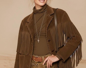 May include: A brown suede jacket with fringe detailing on the sleeves and front. The jacket is paired with a brown turtleneck, matching pants, and a brown belt. A silver necklace and a brown shoulder bag complete the look.