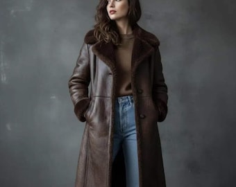 May include: A long, brown leather coat with a shearling lining and collar. The coat has a button closure and pockets. The model is wearing blue jeans and a brown sweater. The coat appears to be knee-length.