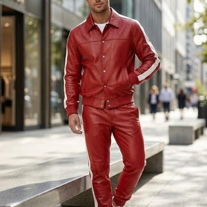 May include: A red leather jacket and trousers set with white side stripes. The jacket features a button closure, and the trousers have a drawstring. The outfit is completed with white trainers. A striking, modern ensemble.