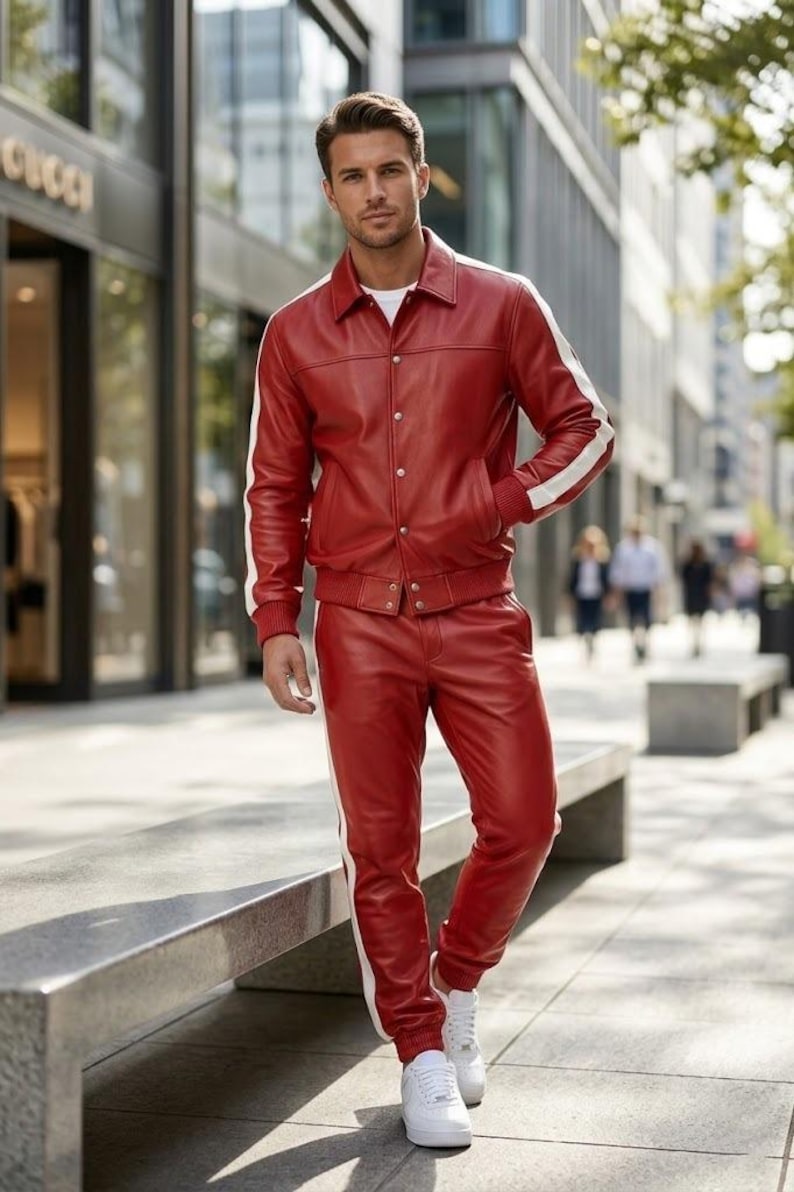 May include: A red leather jacket and trousers set with white side stripes. The jacket features a button closure, and the trousers have a drawstring. The outfit is completed with white trainers. A striking, modern ensemble.