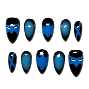 Pode incluir: Um conjunto de dez unhas postiças de vários tamanhos. As unhas apresentam um design com base preta e detalhes azuis. Algumas unhas têm um efeito gradiente, enquanto outras exibem um design de máscara com uma máscara azul e olhos brancos.
