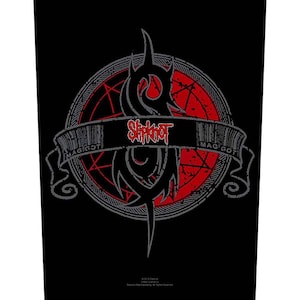 May include: Black graphic with a tribal-style design and a red circle. The word "Slipknot" is in red, and the banner reads "MAGGOT". The design is set against a black background. The image has a grunge aesthetic.