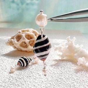 May include: A pair of drop earrings featuring a white pearl at the top, a black and white striped shell in the center, and a small white pearl at the bottom, all connected by silver-toned metal links and findings.