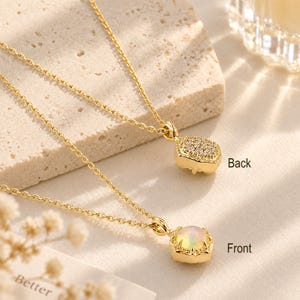 May include: A gold chain necklace featuring two pendants. The front pendant is a round, iridescent opal stone set in a gold frame. The back pendant is a rectangular gold piece encrusted with small clear stones. Text labels read Back and Front.